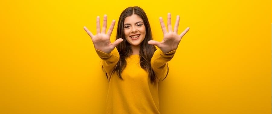 Teenager girl on vibrant yellow background counting ten with fingers